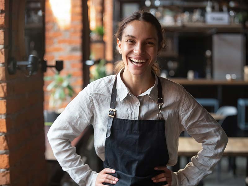smiling woman in black apron in front of a bar