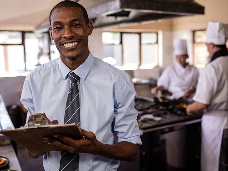 restaurant worker in a tie with chefs cooking in the background